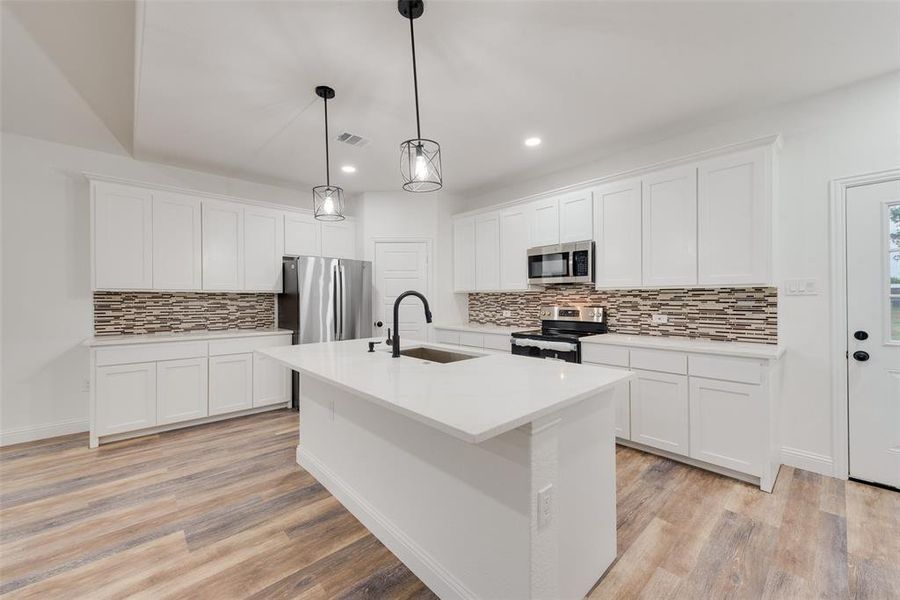 Kitchen featuring hanging light fixtures, sink, white cabinets, appliances with stainless steel finishes, and light hardwood / wood-style floors