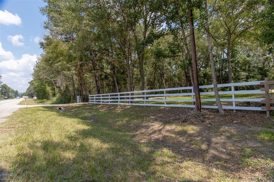 This is FM 1485 roadside property with a white wooden fence and mature trees, offering privacy and a natural setting.