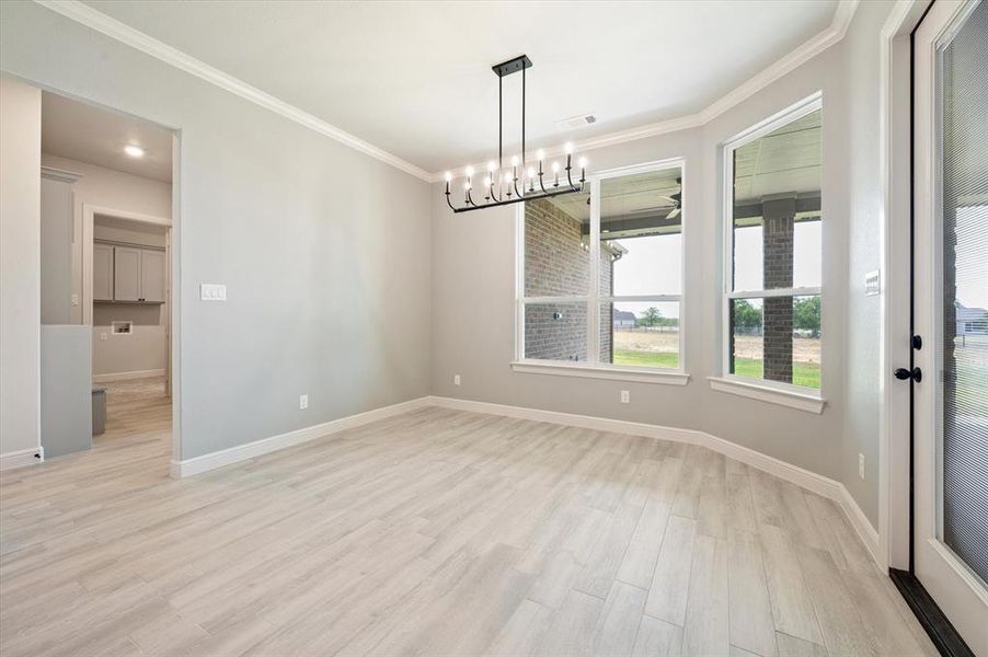 Unfurnished room with light hardwood / wood-style flooring, ornamental molding, and an inviting chandelier