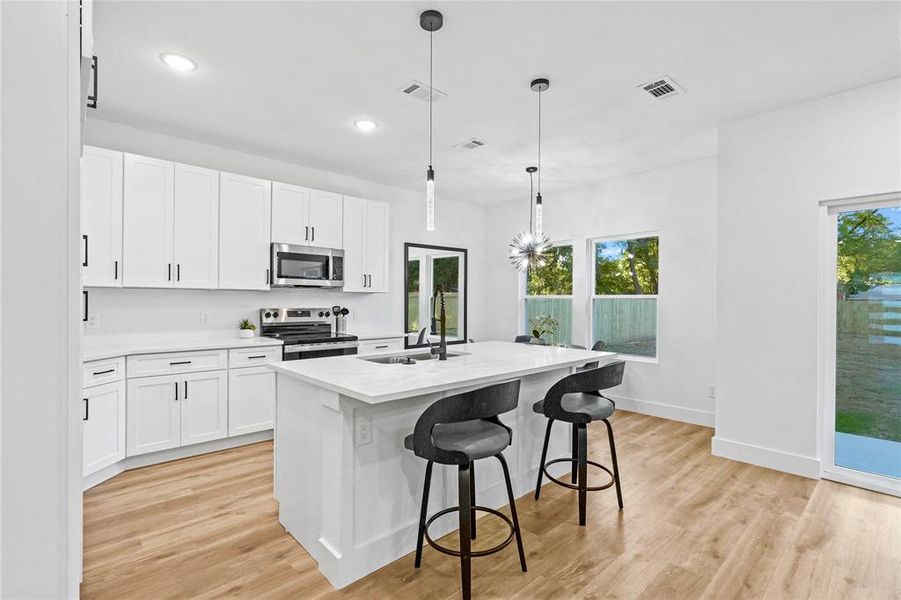 Kitchen featuring white cabinetry, stainless steel appliances, decorative light fixtures, a center island with sink, and sink