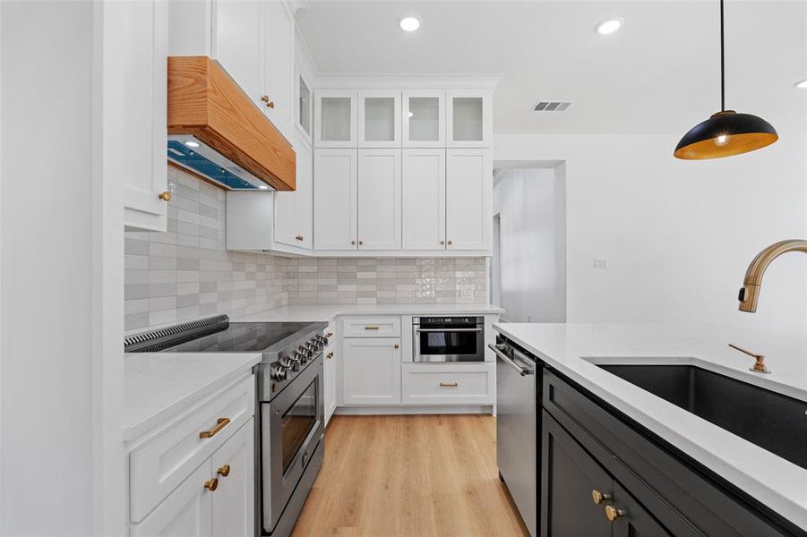 Kitchen featuring light wood-type flooring, stainless steel appliances, hanging light fixtures, and white cabinetry