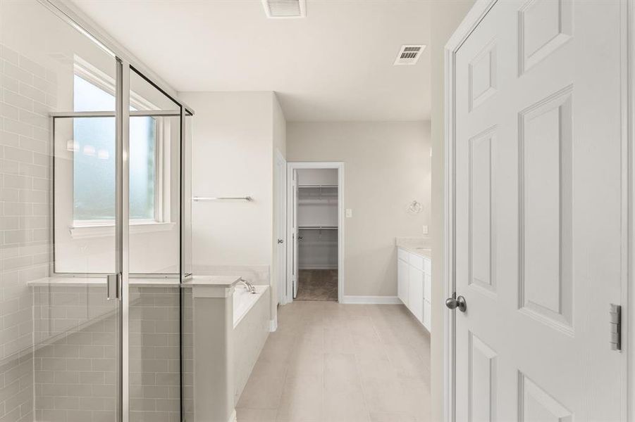 This additional view of your primary bathroom features tile flooring, fresh paint, walk-in shower, a separate garden tub, and a large walk-in closet.