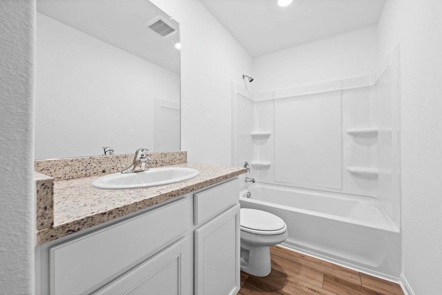 Secondary bathroom includes granite counters, designer white cabinetry and luxury vinyl plank flooring.