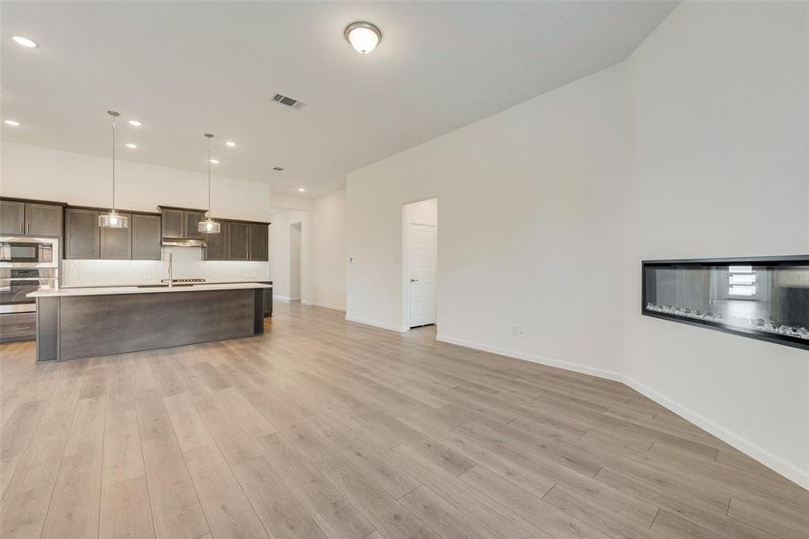 Kitchen with light hardwood / wood-style flooring, appliances with stainless steel finishes, dark brown cabinets, an island with sink, and pendant lighting