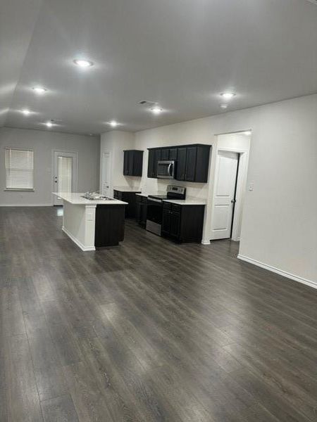 Kitchen featuring stainless steel range with electric cooktop, sink, a center island with sink, and dark hardwood / wood-style flooring