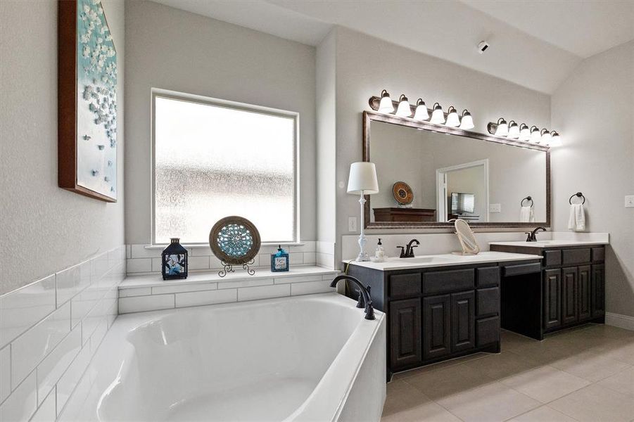 Bathroom with a bath to relax in, dual bowl vanity, tile floors, and lofted ceiling