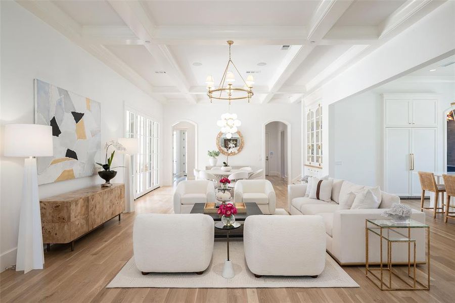 Living room with an inviting chandelier, coffered ceiling, and light wood flooring
