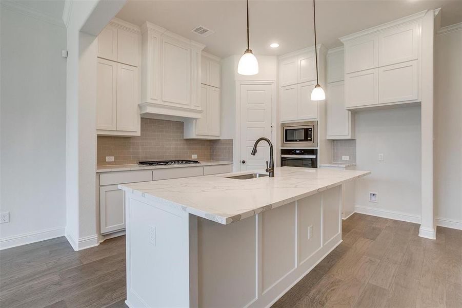 Kitchen with decorative backsplash, sink, light hardwood / wood-style floors, appliances with stainless steel finishes, and a kitchen island with sink