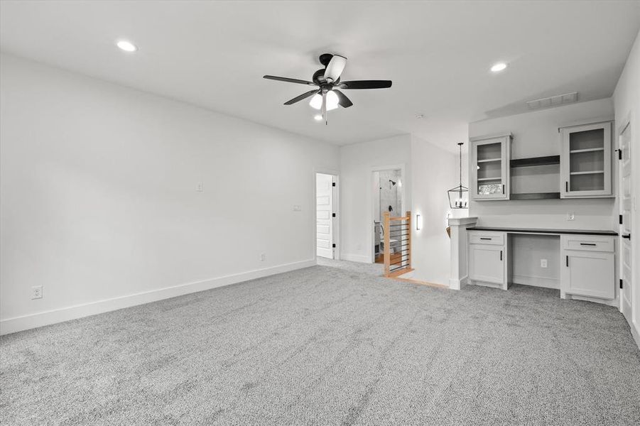 Unfurnished living room featuring light colored carpet, built in desk, and ceiling fan