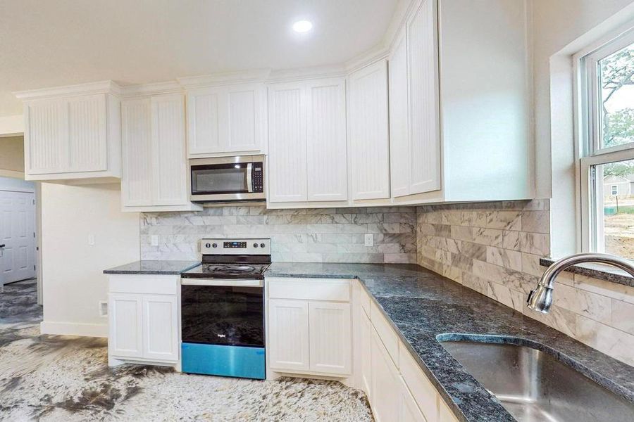 Kitchen featuring white cabinets, sink, stainless steel appliances, and tasteful backsplash