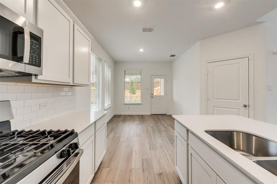 Kitchen with white cabinets, backsplash, light wood-type flooring, appliances with stainless steel finishes, and sink