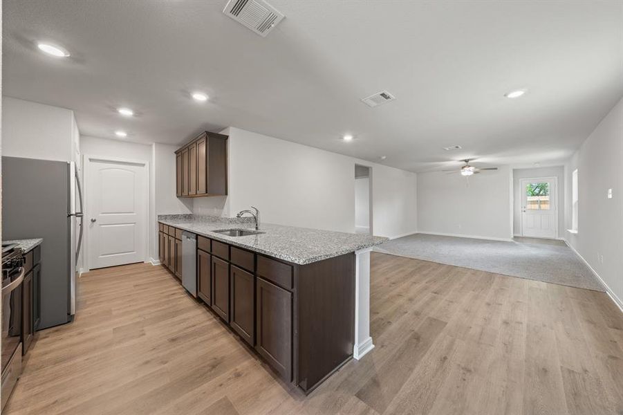 Kitchen featuring light wood-type flooring, light stone countertops, sink, kitchen peninsula, and ceiling fan