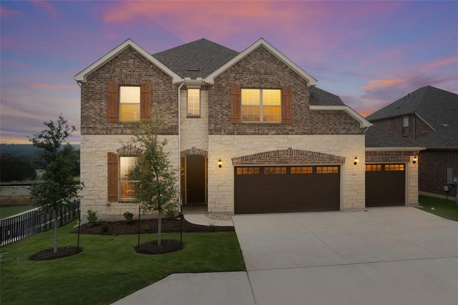 Virtual shot of home at dusk. Attractive brick/stone exterior with wooden shutters and 3-car garage.