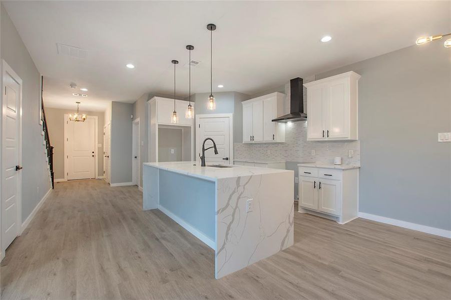 Kitchen featuring an island with sink, light wood-type flooring, wall chimney range hood, and white cabinets