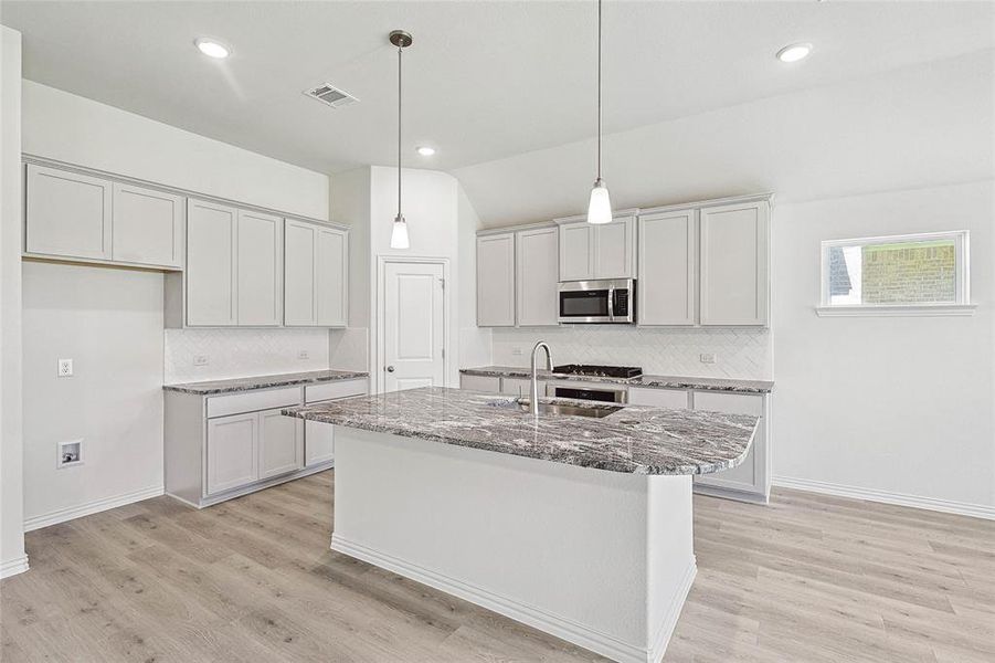 Kitchen with pendant lighting, a kitchen island with sink, sink, tasteful backsplash, and light hardwood / wood-style flooring