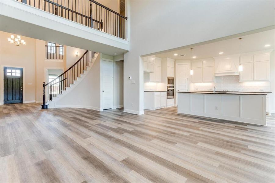 Unfurnished living room with sink, an inviting chandelier, a high ceiling, and light hardwood / wood-style floors