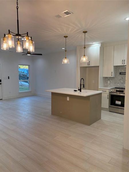 Kitchen with hanging light fixtures, a center island with sink, white cabinetry, stove, and light hardwood / wood-style flooring