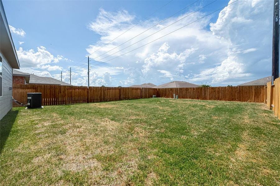 A spacious backyard with green grass and wooden fence.