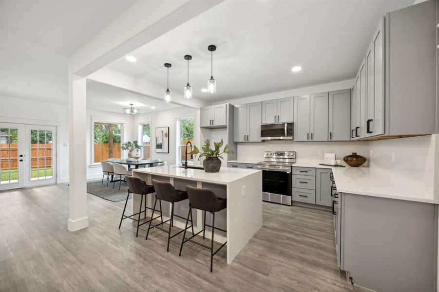 Kitchen with gray cabinetry, a center waterfall island with sink, stainless steel appliances and a pantry