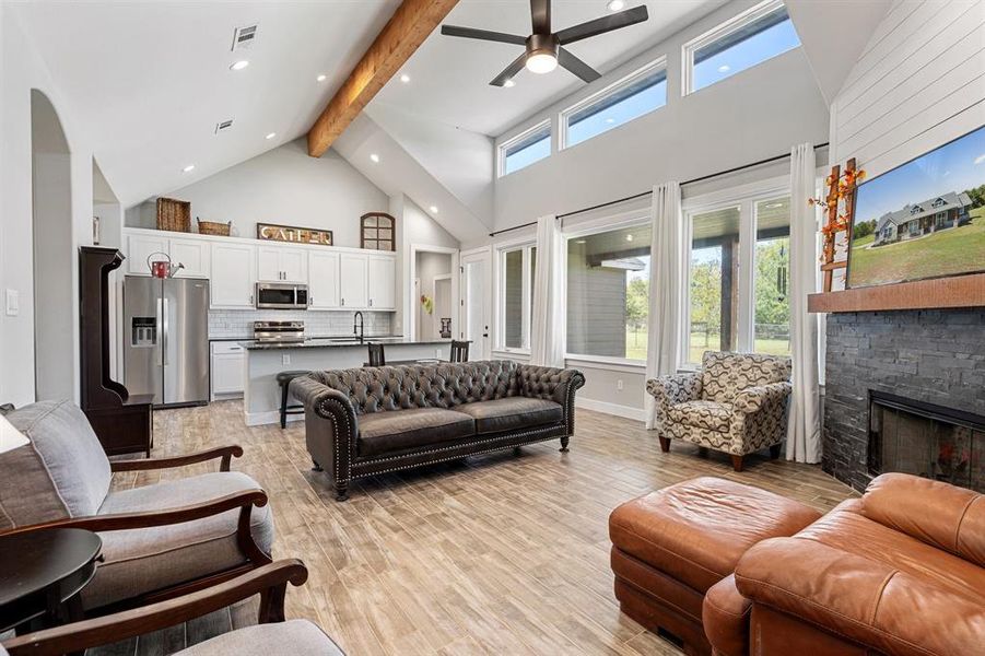 Living room with ceiling fan, beamed ceiling, a stone fireplace, light hardwood / wood-style flooring, and high vaulted ceiling