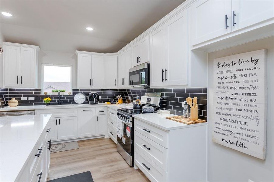 Kitchen featuring decorative backsplash, white cabinets, stainless steel appliances, and light wood-type flooring