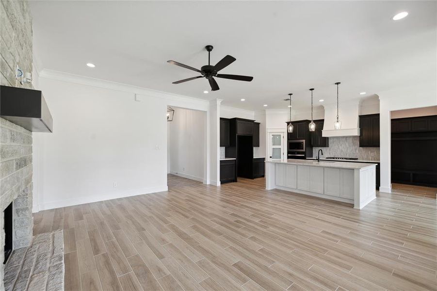 Kitchen with light hardwood / wood-style flooring, a kitchen island with sink, a stone fireplace, ceiling fan, and tasteful backsplash