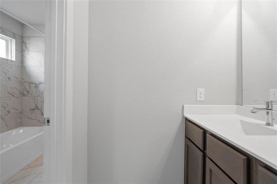 Secondary bath features a private vanity area and then opens to a shared tub/shower combo and toilet. Features include tile flooring, bath/shower combo with tile surround, wood stained cabinets, beautiful light countertops, mirror, dark, sleek fixtures and modern finishes!