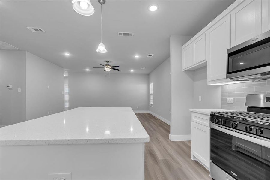 Kitchen featuring hanging light fixtures, white cabinetry, stainless steel appliances, ceiling fan, and light hardwood / wood-style flooring