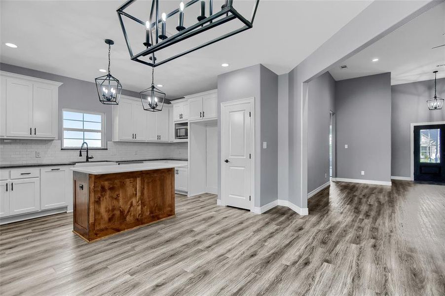 Kitchen with decorative light fixtures, tasteful backsplash, a kitchen island, and light hardwood / wood-style flooring