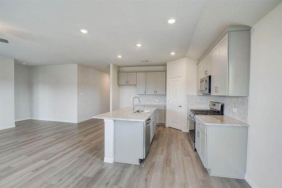 Kitchen featuring light stone counters, a kitchen island with sink, appliances with stainless steel finishes, and light hardwood / wood-style flooring