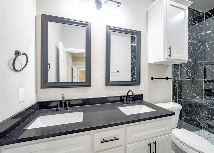 Bathroom with a tile shower, dual sinks, oversized vanity, and toilet