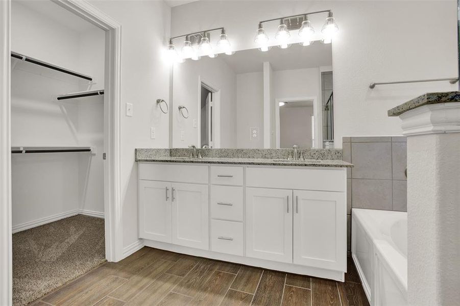Bathroom with a tub, wood-type flooring, oversized vanity, and dual sinks