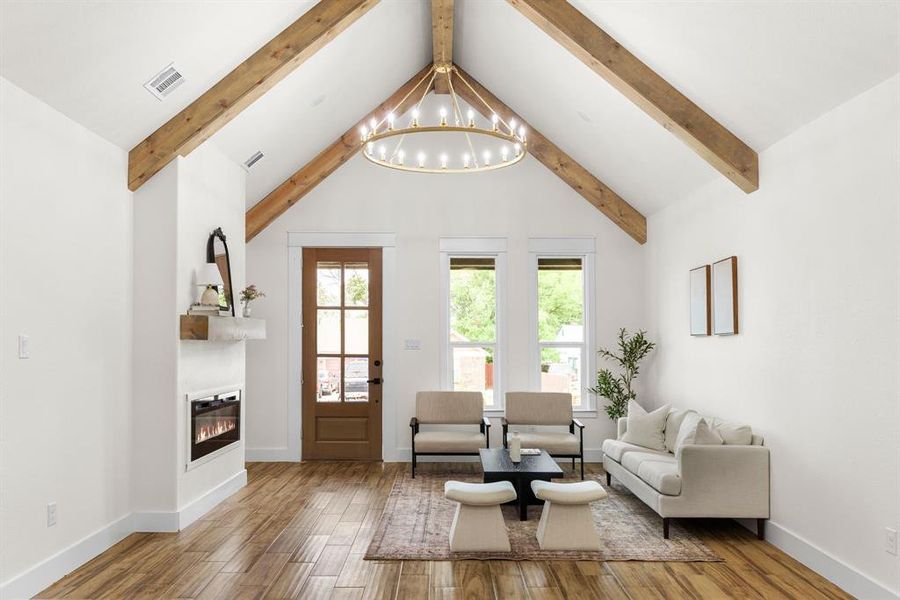 Living room featuring beam ceiling, a notable chandelier, hardwood / wood-style floors, and high vaulted ceiling