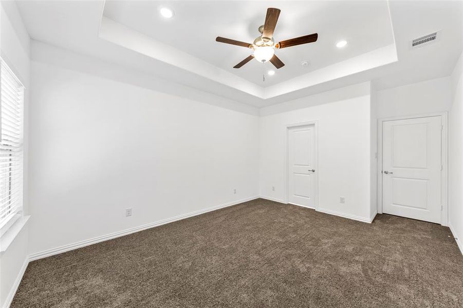 Unfurnished bedroom featuring a tray ceiling, ceiling fan, and dark carpet