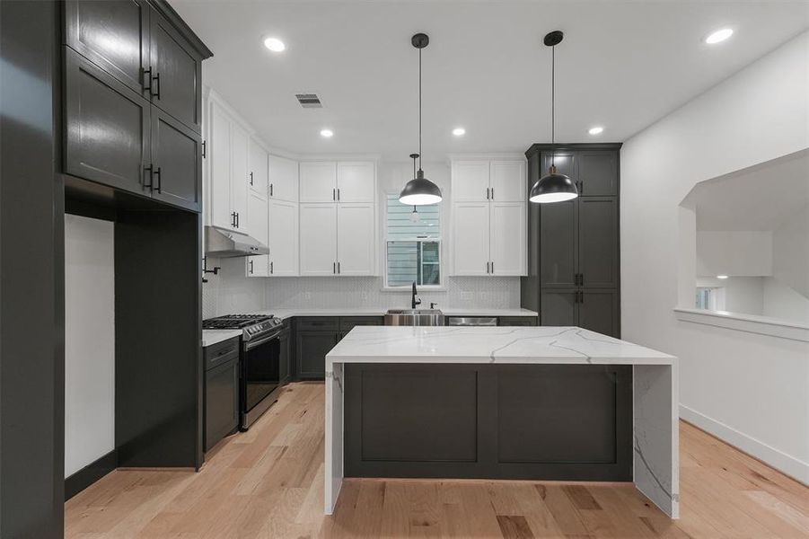 Modern kitchen featuring white countertops, custom dark cabinetry, stainless steel appliances, a central island, and engineered hardwood floors.