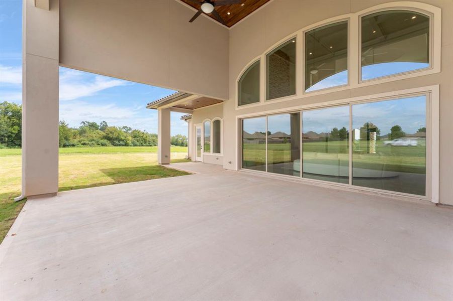 Spacious covered patio with large arched windows offering an expansive view of the lush green lawn, perfect for indoor-outdoor living.