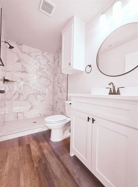 Bathroom featuring wood-type flooring, a tile shower, vanity, and toilet