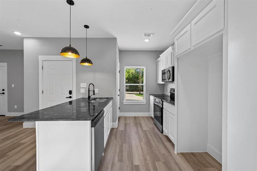 Kitchen with appliances with stainless steel finishes, white cabinets, pendant lighting, light hardwood / wood-style flooring, and sink