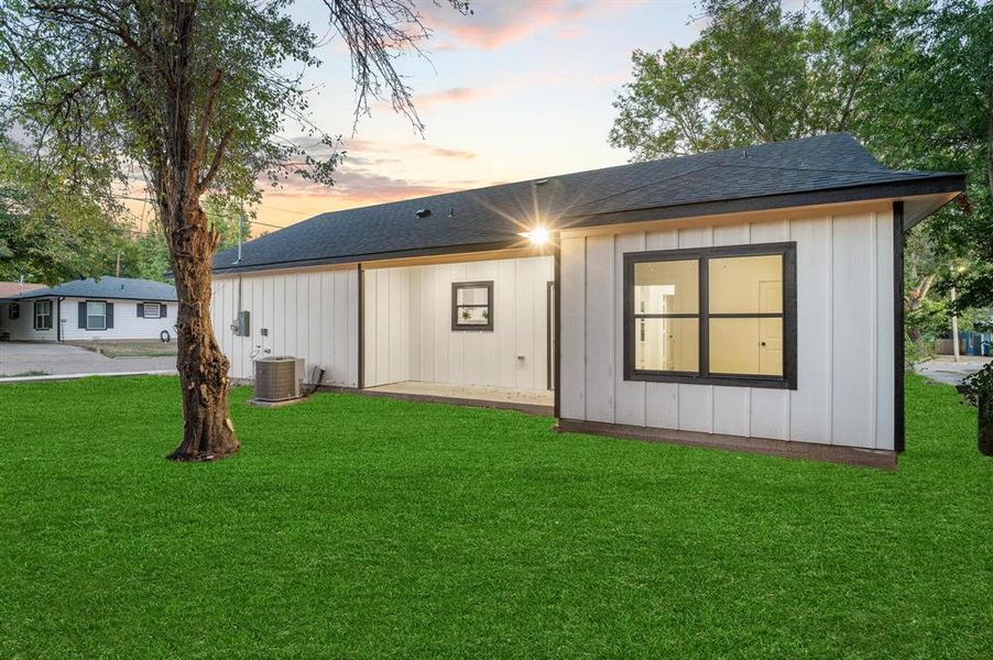 Back house at dusk featuring a lawn and cooling unit