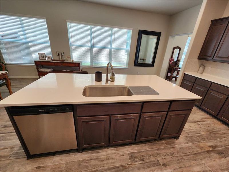 Kitchen featuring light style floors, dark brown cabinetry, a center island with sink, sink, and dishwasher