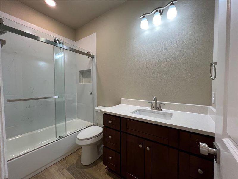 Full bathroom with bath / shower combo with glass door, hardwood / wood-style flooring, vanity, and toilet