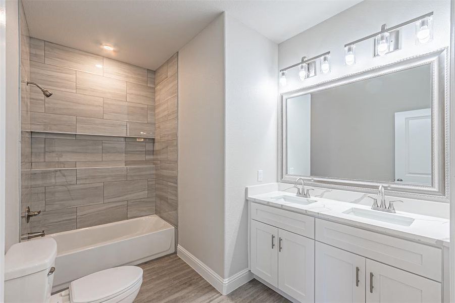Full bathroom featuring toilet, hardwood / wood-style floors, tiled shower / bath, and dual bowl vanity