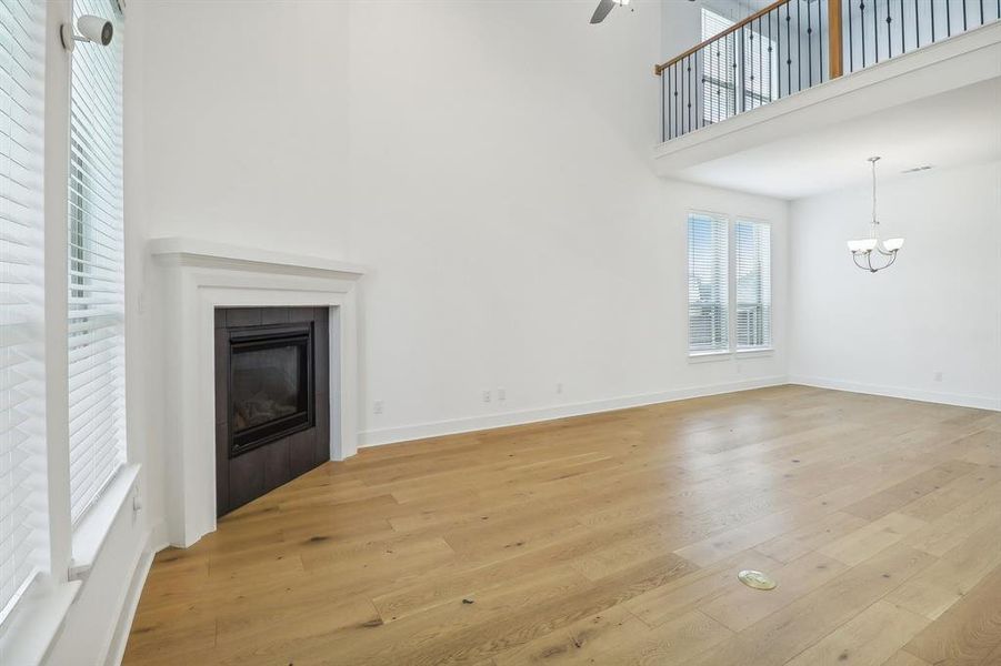 Unfurnished living room featuring a high ceiling, light hardwood / wood-style flooring, ceiling fan with notable chandelier, and a tile fireplace