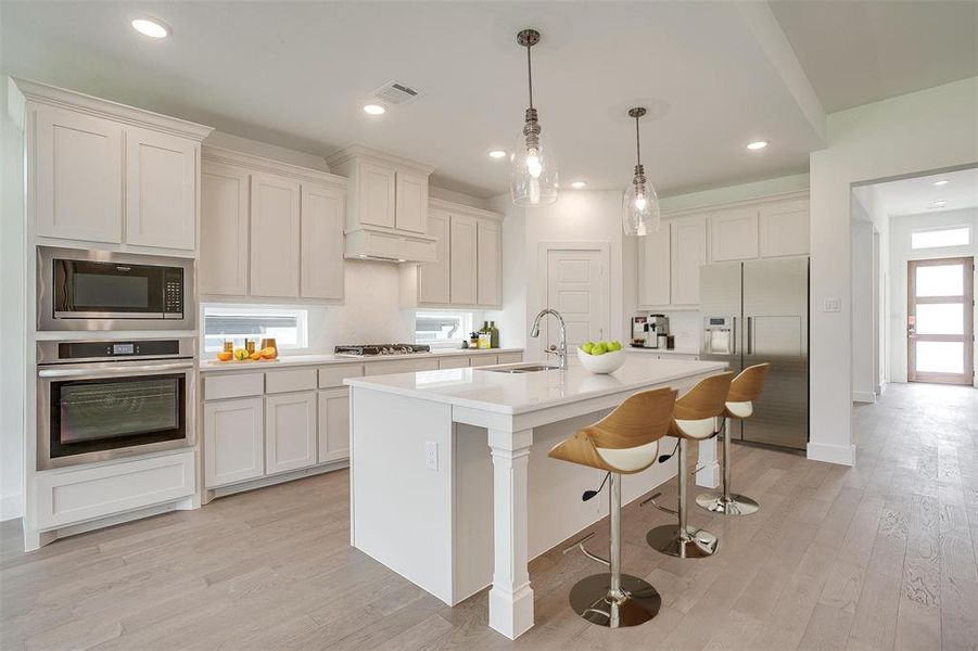 Kitchen featuring a center island with sink, light hardwood / wood-style flooring, appliances with stainless steel finishes, white cabinets, and sink