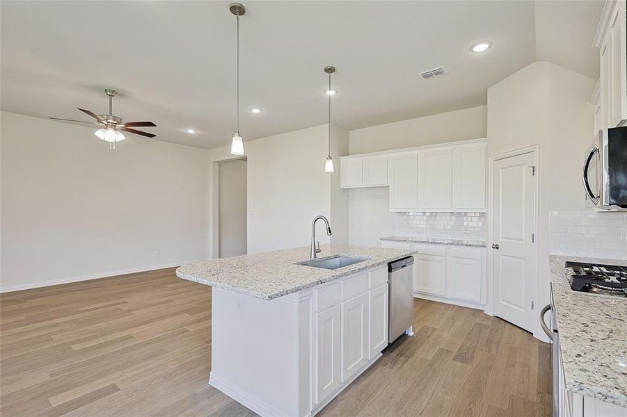 Kitchen featuring tasteful backsplash, appliances with stainless steel finishes, white cabinetry, light hardwood / wood-style floors, and a kitchen island with sink