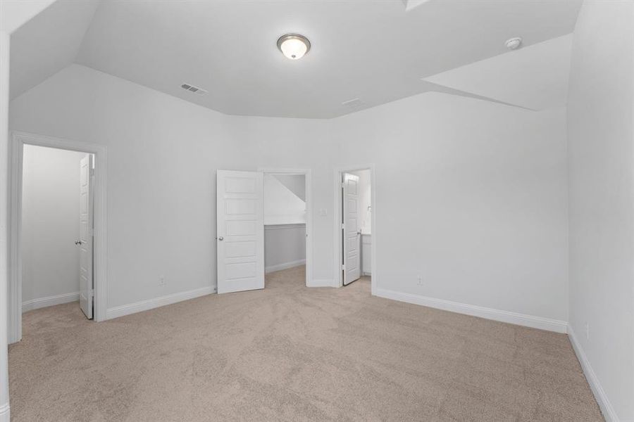 Unfurnished bedroom featuring a closet, ensuite bathroom, a walk in closet, light colored carpet, and lofted ceiling