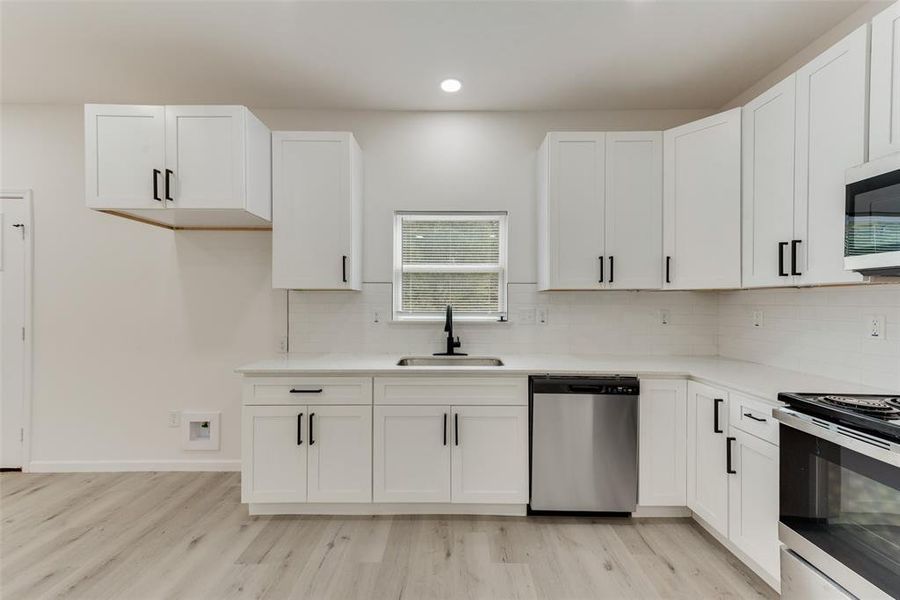 Kitchen with white cabinets, light wood-type flooring, stainless steel appliances, sink, and decorative backsplash