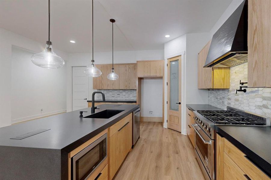 Kitchen with sink, light hardwood / wood-style floors, pendant lighting, wall chimney range hood, and appliances with stainless steel finishes