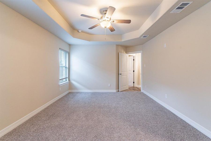 Carpeted empty room featuring a tray ceiling and ceiling fan