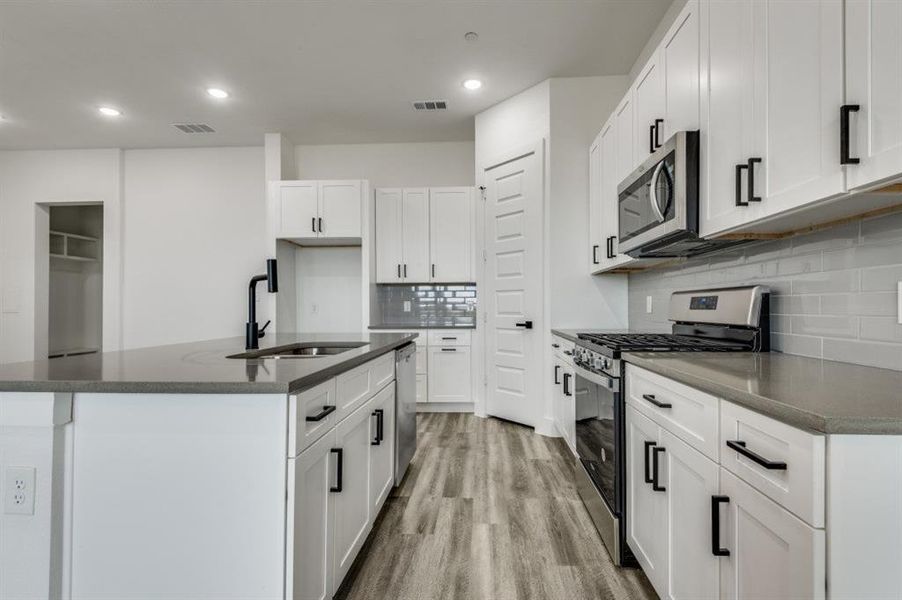 Kitchen with white cabinets, sink, a kitchen island with sink, light wood-type flooring, and appliances with stainless steel finishes